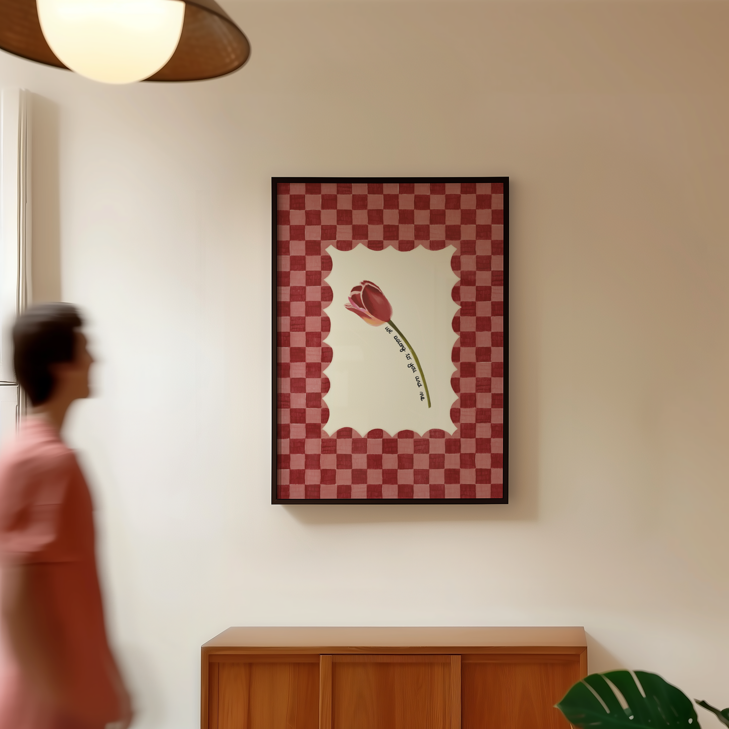 Framed artwork with a red tulip design on a wall, with a person and plant in the foreground.